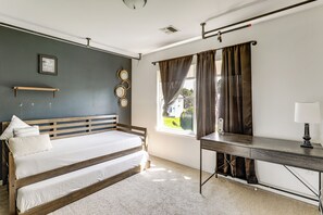 Un dormitorio con cama, escritorio, ventana con cortinas, espejo montado en la pared y un marco de fotos.