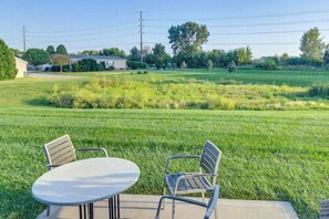 An outdoor seating area with a table and two chairs, surrounded by a grassy field and a residential neighborhood.