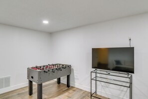 A room with a foosball table and a TV on a stand.