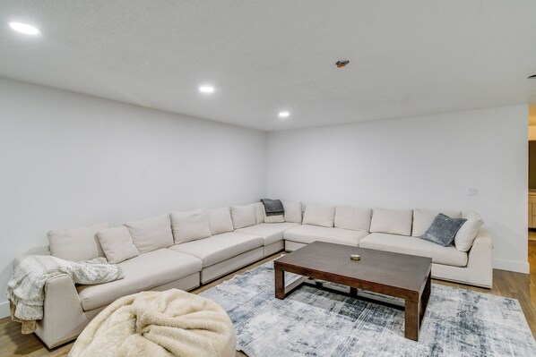 A modern living room with a large L-shaped sectional sofa, a wooden coffee table, and a shaggy pouf.
