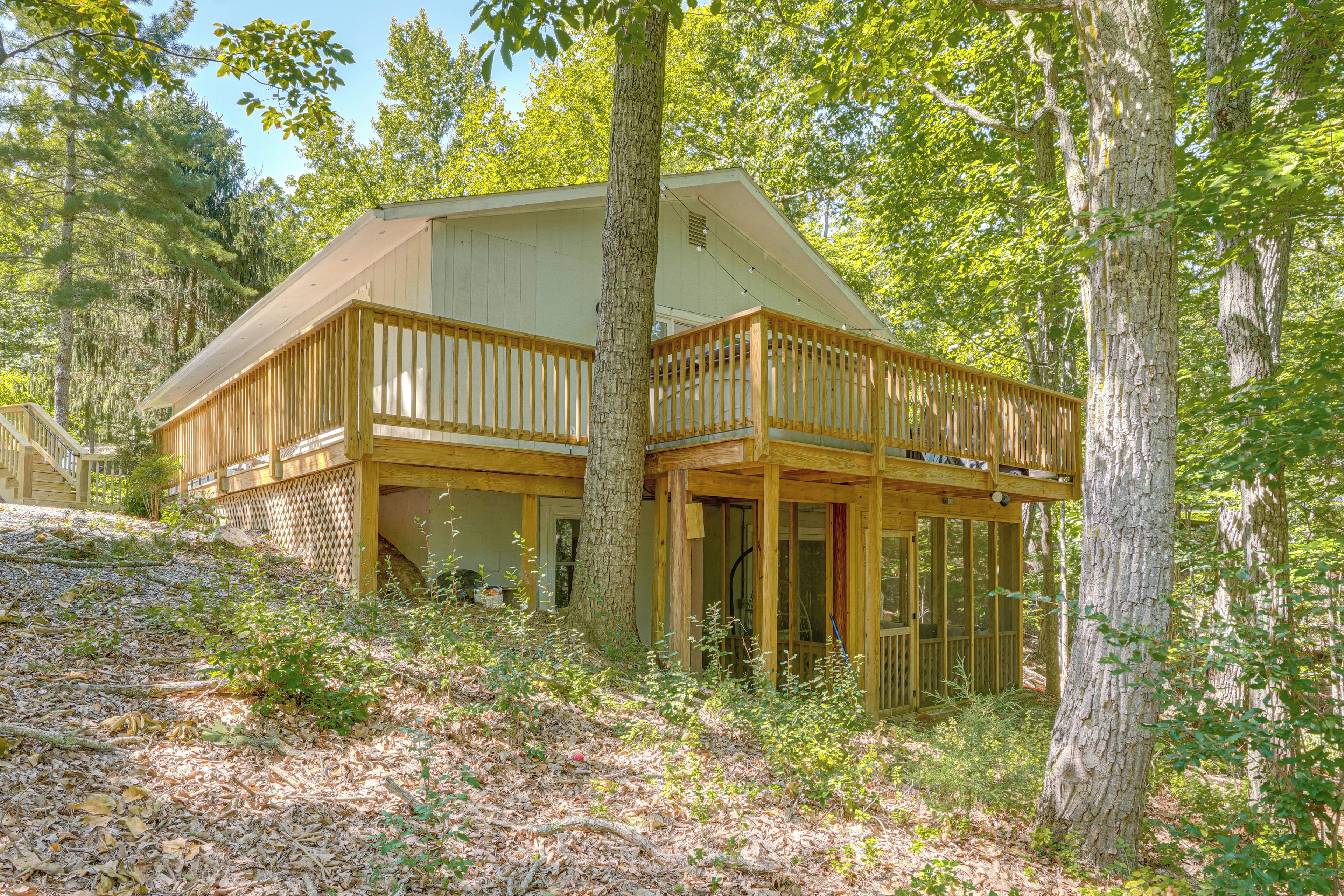 A cabin with a wooden deck and a covered porch, surrounded by trees and natural ground cover.