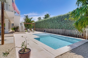 A swimming pool with a wooden deck, a pergola, and a view of a residential building with an American flag. - Private Dock & Pool: Waterfront Key Largo Home (Key Largo)
