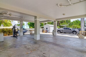 Uma área externa coberta com piso de concreto, uma bicicleta ergométrica fixa, uma motorhome coberta e uma caminhonete estacionada.