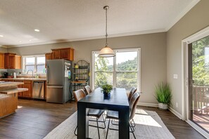 A spacious kitchen with a dining area, wooden cabinets, a stainless steel refrigerator, and a large window offering a view of greenery. - Hiking Days, Campfire Nights! Hot Springs Hideaway (Hot Springs)