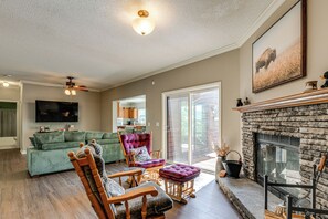 A spacious living room with a green sofa, wooden chairs, a fireplace, and a television mounted on the wall. - Hiking Days, Campfire Nights! Hot Springs Hideaway (Hot Springs)