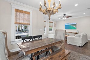 A dining area with a wooden table and chairs, a chandelier, and a view of the outdoors through large windows. - Vitamin Sea- VCB (Destin)