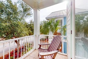 A covered balcony with a wooden chair, a small table, and a view of a house and trees. - Vitamin Sea- VCB (Destin)