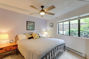 Ein Schlafzimmer mit Bett, Nachttischlampen, einer Uhr, einem Deckenventilator und einem Fenster mit Blick auf Grünflächen.