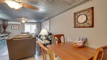 A living room with a leather sofa, a wooden dining table, a wall clock, and a framed picture.