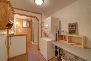 Cozinha compacta com máquina de lavar, pia pequena e janela com cortinas.