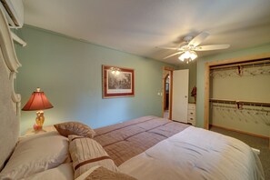 Quarto com cama, ventilador de teto, quadro na parede e closet espaçoso com cabides.