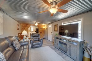 Ein Wohnzimmer mit einer Ledersofa, Deckenventilator aus Holz, einem Fernseher und einem Kamin.