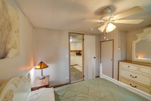 A bedroom with a bed, a nightstand, a lamp, a ceiling fan, a dresser, and a mirror. - Lake Country Retreat Near Eufaula Adventures (Eufaula)