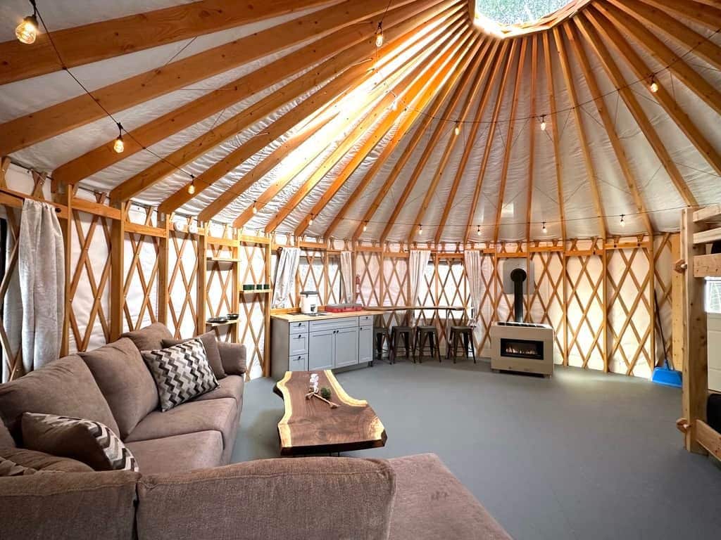 A yurt interior with a sofa, wooden table, kitchen area, and a chimney.