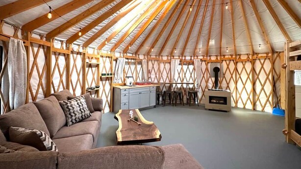 A yurt interior with a sofa, wooden table, kitchen area, and a chimney.