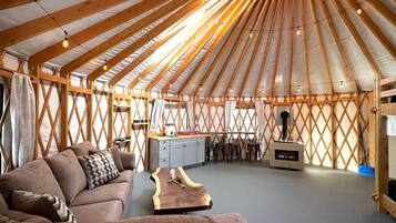 A yurt interior with a sofa, wooden table, kitchen area, and a chimney.