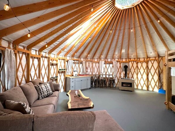 A yurt interior with a sofa, wooden table, kitchen area, and a chimney.