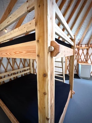 A wooden bunk bed with a black mattress, a wooden headboard, and a ladder.