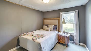 A bedroom with a bed, a nightstand, a lamp, and a window with curtains.