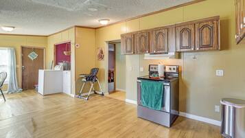 A compact kitchen with wooden cabinets, a refrigerator, a stove, and a chair.