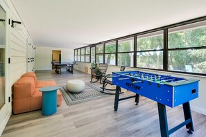 A modern living room with a foosball table, a sofa, a coffee table, and a view through large windows. - Pelican House: Waterfront w/ Paddleboat and Kayaks (Homosassa)
