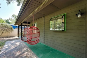 A covered porch with a green floor, a red hanging chair, and a window with a green frame. - Pelican House: Waterfront w/ Paddleboat and Kayaks (Homosassa)