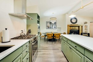 Cozinha moderna com armários verdes, bancada branca e área de refeições com mesa e cadeiras redondas.