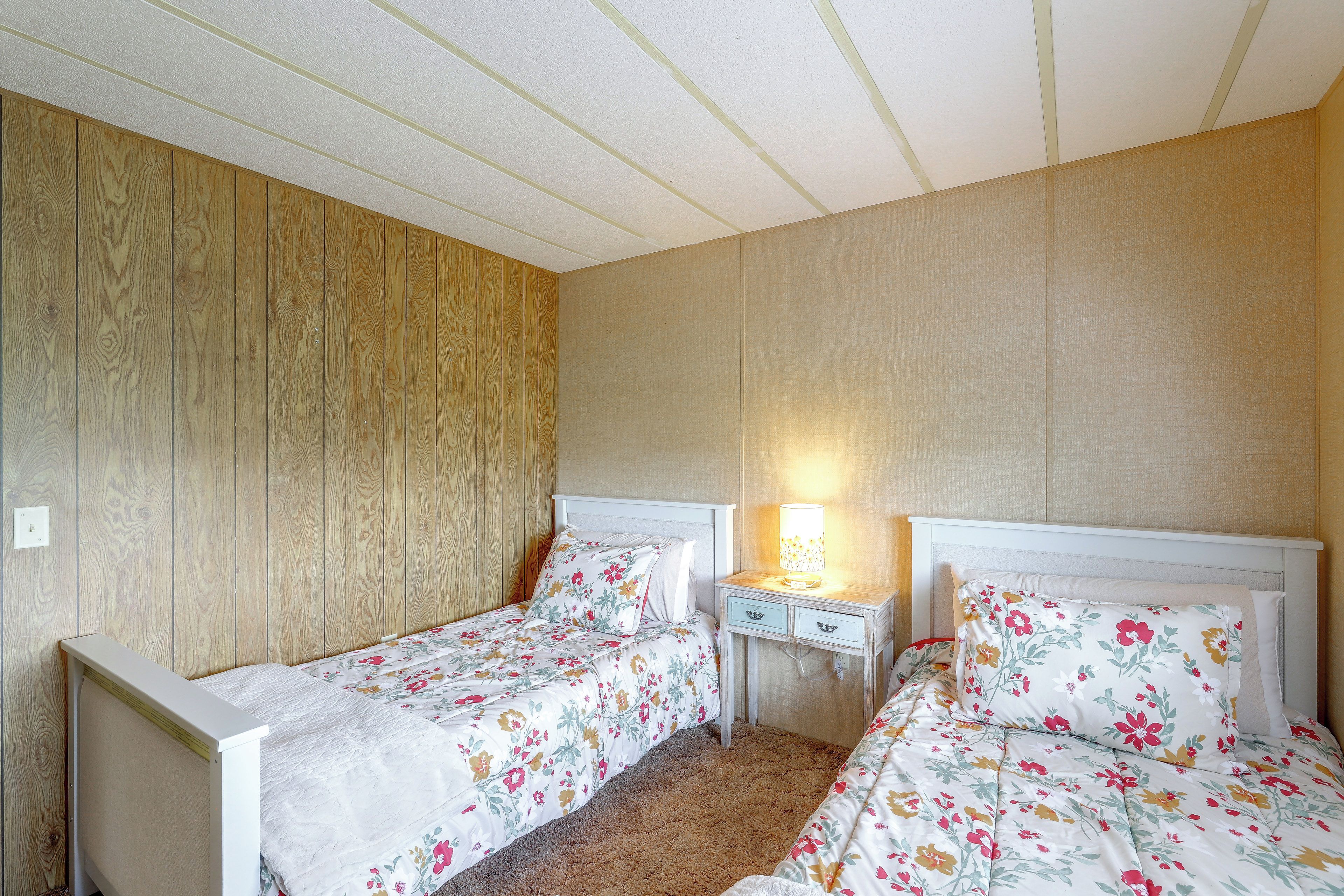 A bedroom with two single beds, a nightstand with a lamp, and a wooden panel wall.