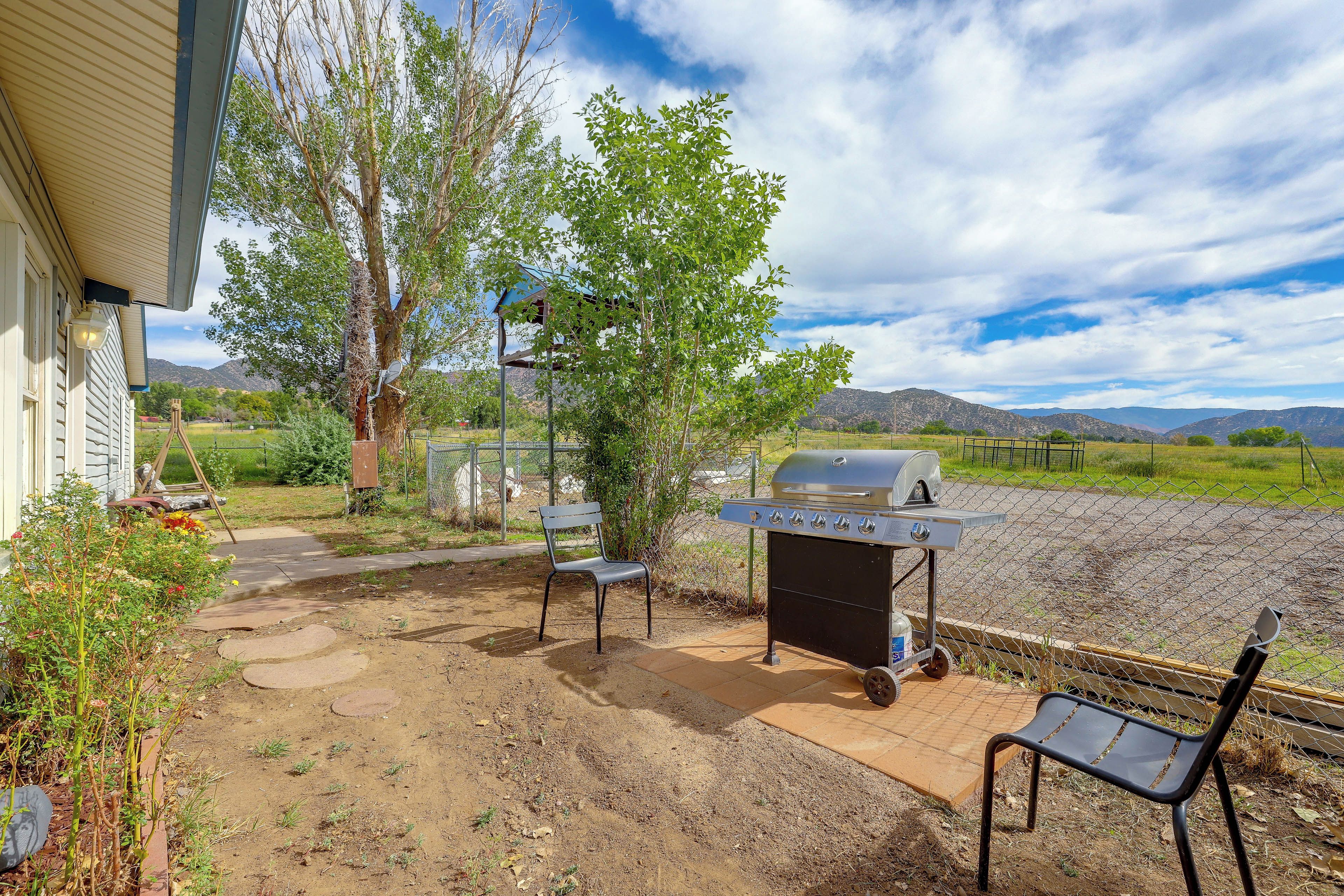An outdoor patio with a grill, a bench, and a pathway leading to a house.