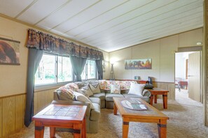 A cozy living room with a sectional sofa, two wooden tables, and a large window with curtains.