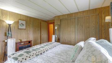 A bedroom with wooden panel walls, a bed with patterned bedding, a nightstand, a lamp, and a framed picture.