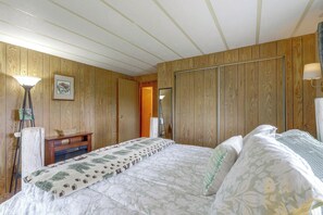A bedroom with wooden panel walls, a bed with patterned bedding, a nightstand, a lamp, and a framed picture.