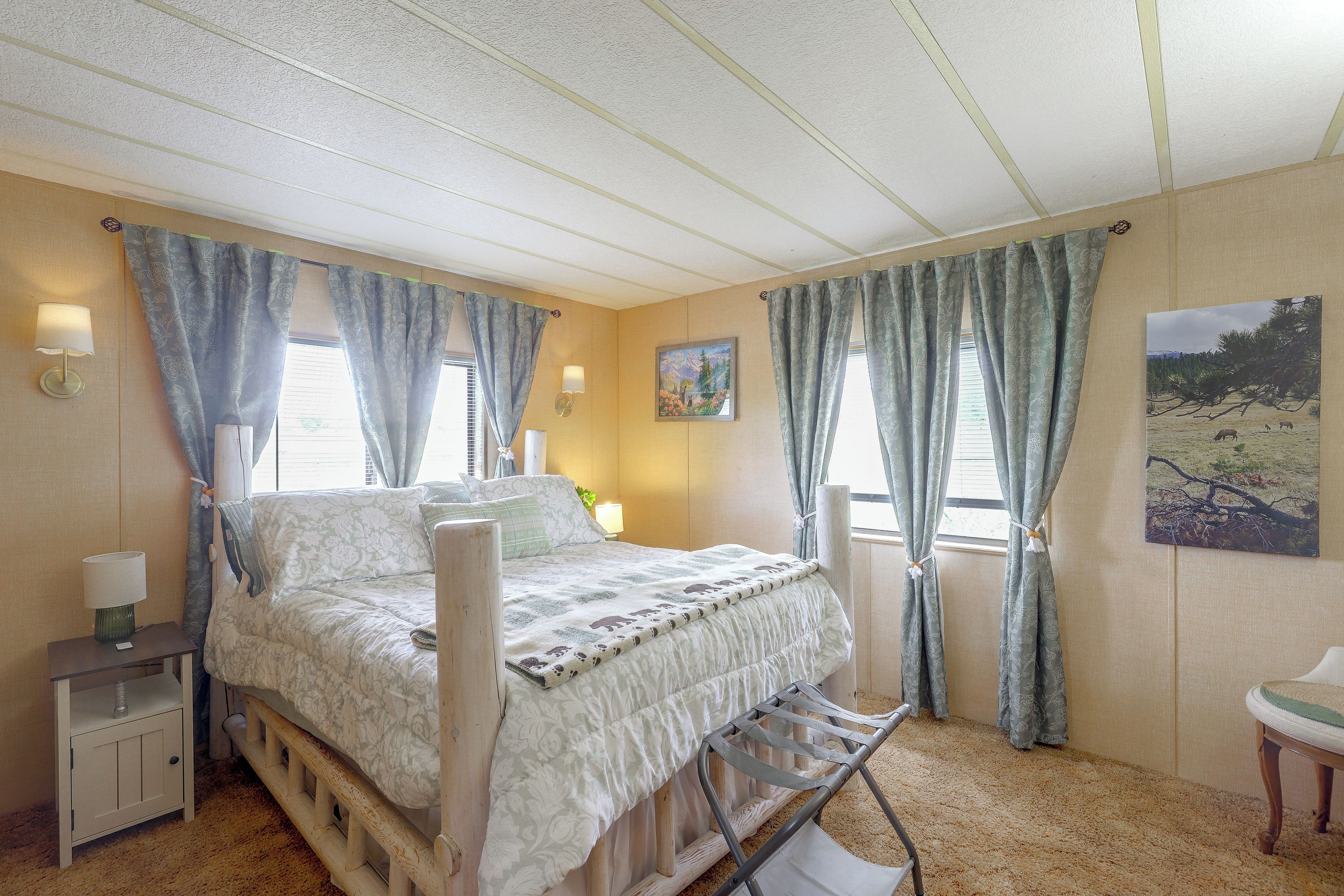A bedroom with a bed, bedside lamps, a nightstand, a window with curtains, and a painting on the wall.