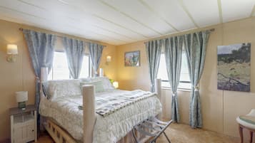 A bedroom with a bed, bedside lamps, a nightstand, a window with curtains, and a painting on the wall.