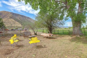 An outdoor seating area with yellow chairs and a picnic table, surrounded by trees and a mountain in the background.