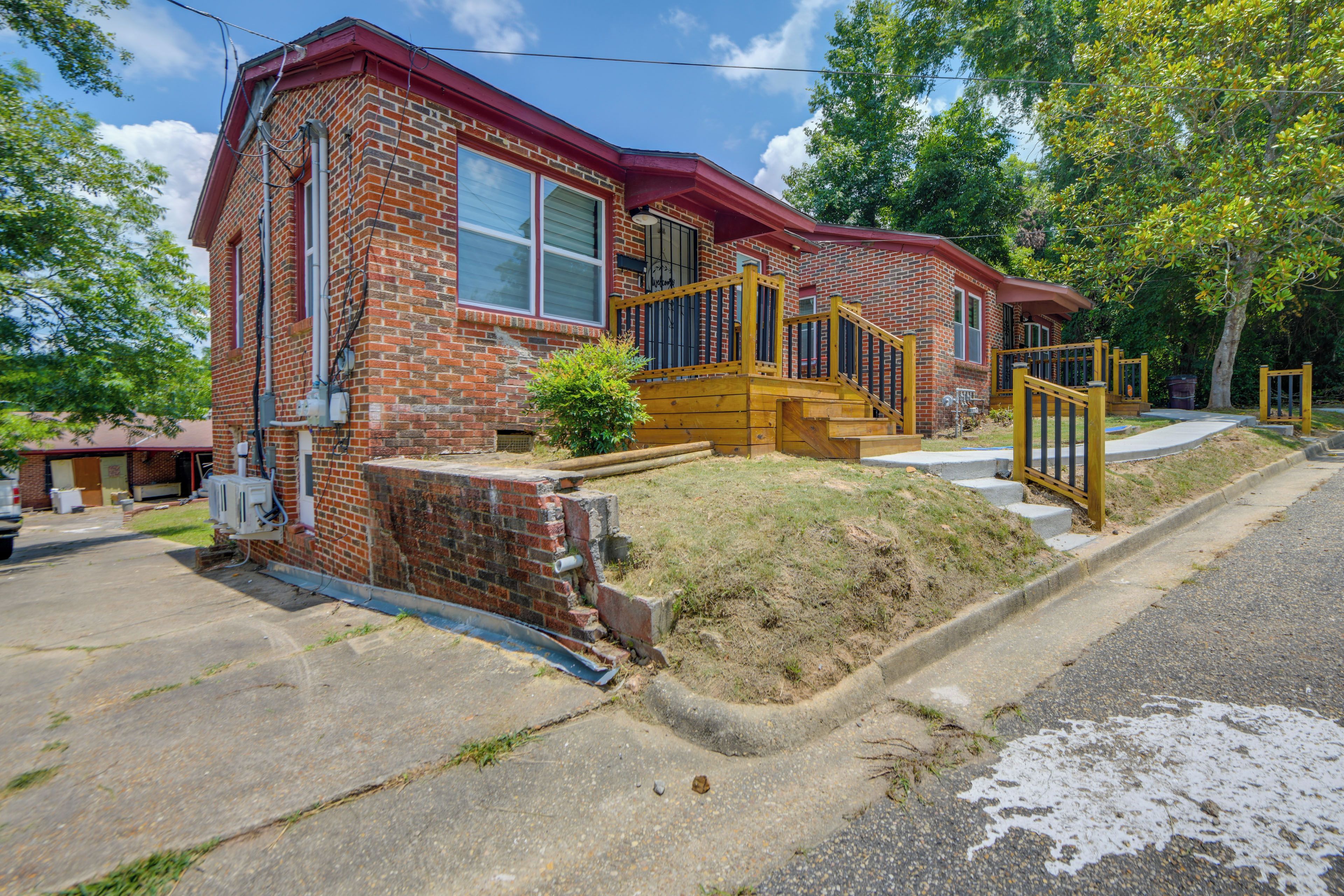 A two-story brick house with a red roof, a front porch, and a wooden staircase leading to the entrance.