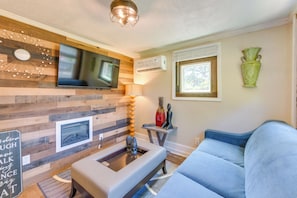 Uma sala de estar moderna com televisão de tela plana, lareira, sofá e um detalhe decorativo na parede.