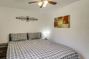 A bedroom with a bed, a ceiling fan, a wall-mounted light, and a piece of wall art.