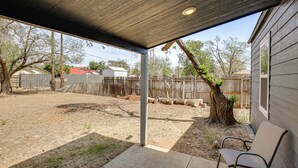 A covered patio area with a concrete floor, a metal chair, and a wooden fence in the background. - 1 Mi to Dtwn! Lubbock Home w/ Private Patio & Yard (Lubbock)