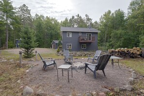 A two-story house with a balcony, surrounded by a gravel patio with outdoor furniture. - Secluded Hayward Cabin With Hot Tub/on Trailhead (Hayward)