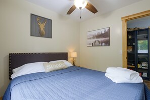 A neatly made bed with a blue quilt, a pillow with 'SUMMER' text, a ceiling fan, and a bookshelf with various items. - Secluded Hayward Cabin With Hot Tub/on Trailhead (Hayward)