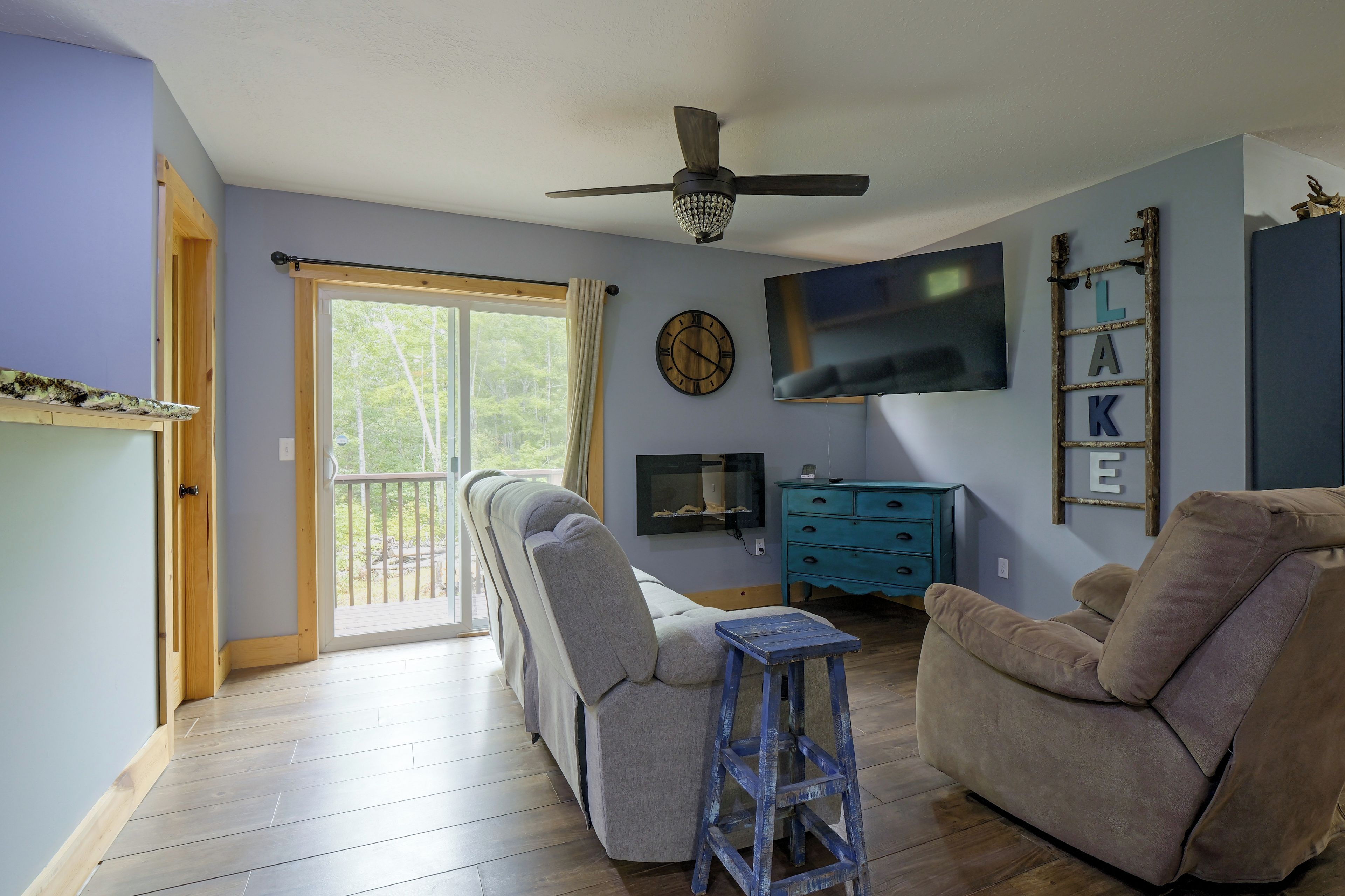 A living room with a ceiling fan, a flat-screen TV, a clock, and a blue dresser.