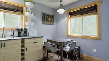 A modern kitchen with a dining area, wooden cabinets, a sink, and a window with a view of trees.
