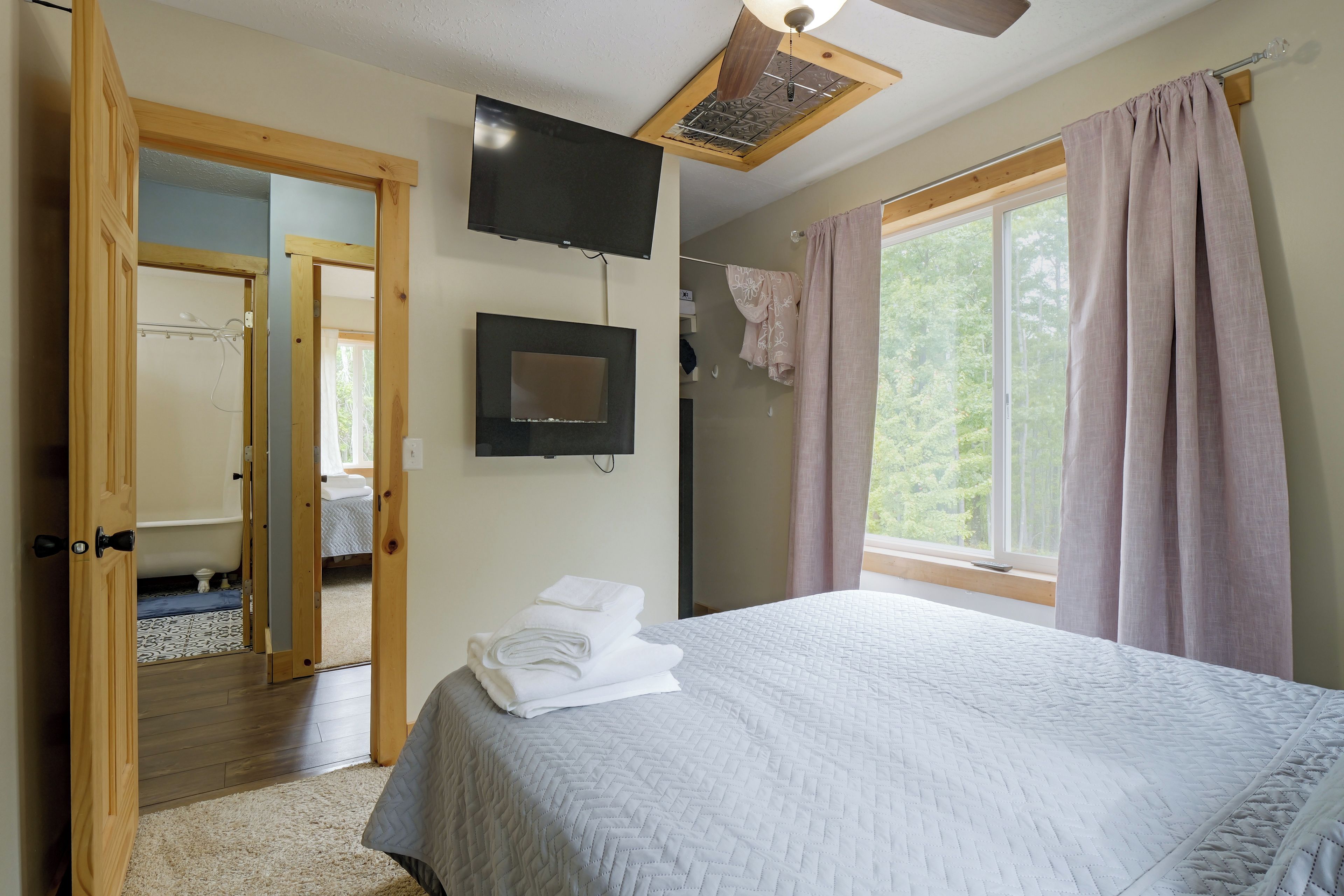 A bedroom with a bed, a television, a window with curtains, and a door leading to a bathroom.