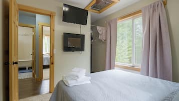 A bedroom with a bed, a television, a window with curtains, and a door leading to a bathroom.