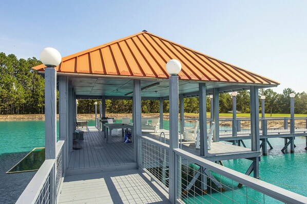 A covered outdoor area with a roof, seating, and a railing overlooking a body of water.
