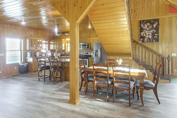 A spacious kitchen with wooden cabinets, a dining area with a large table and chairs, and a staircase leading to an upper level.