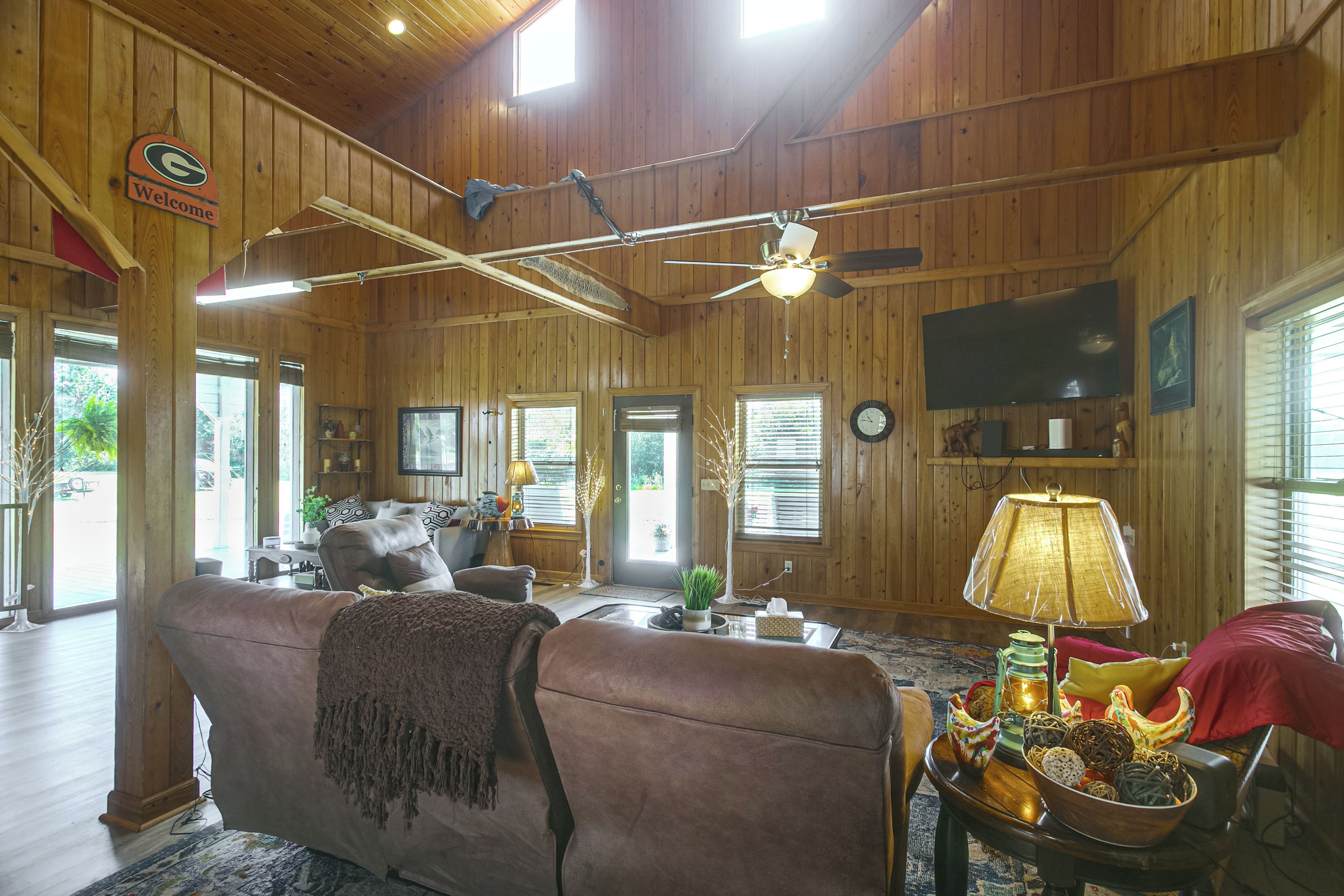 A spacious living room with a large couch, a television mounted on the wall, and a ceiling fan.