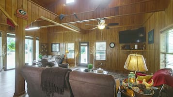 A spacious living room with a large couch, a television mounted on the wall, and a ceiling fan.
