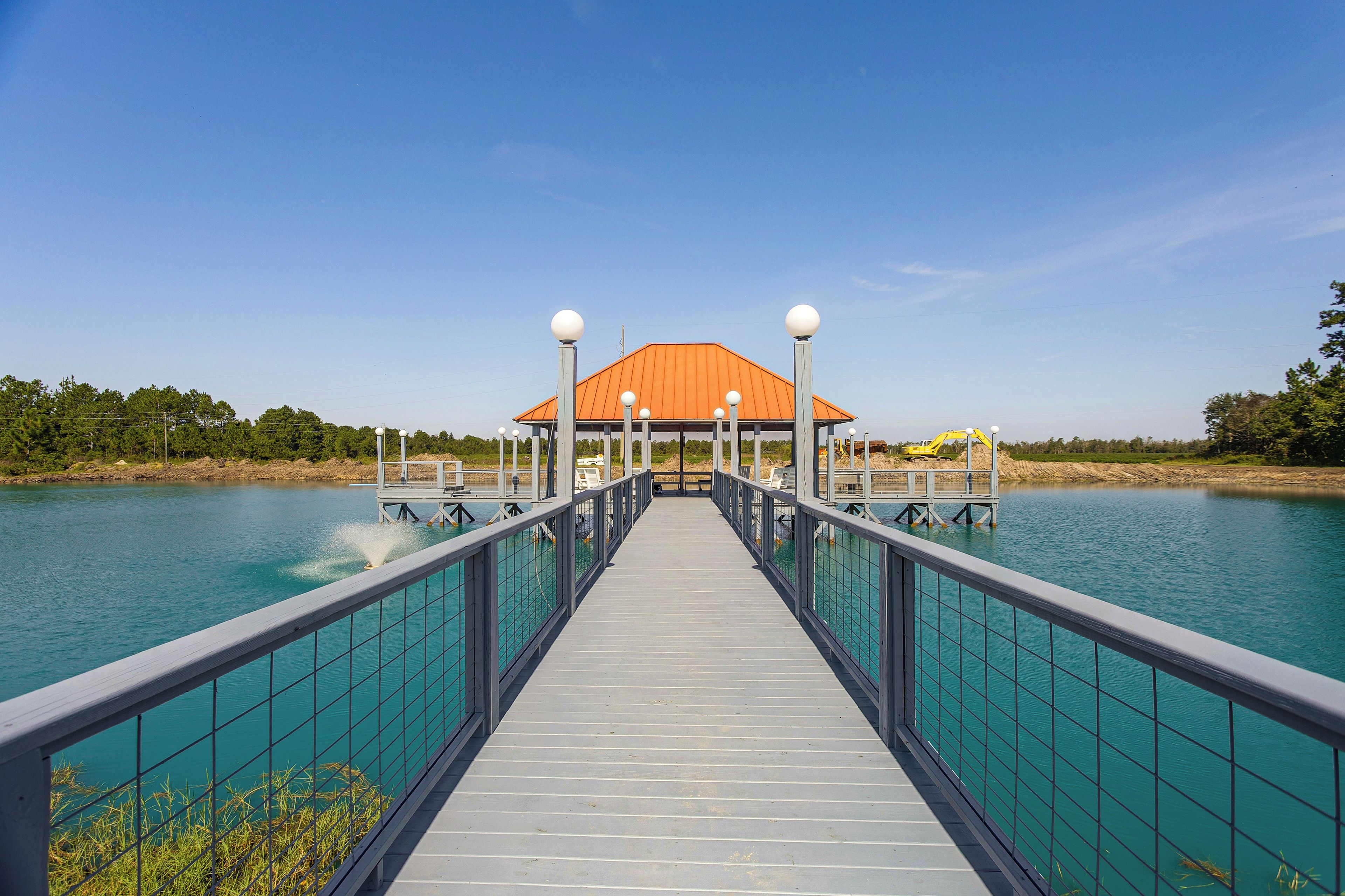 A pier leading to a building with a red roof, surrounded by water.